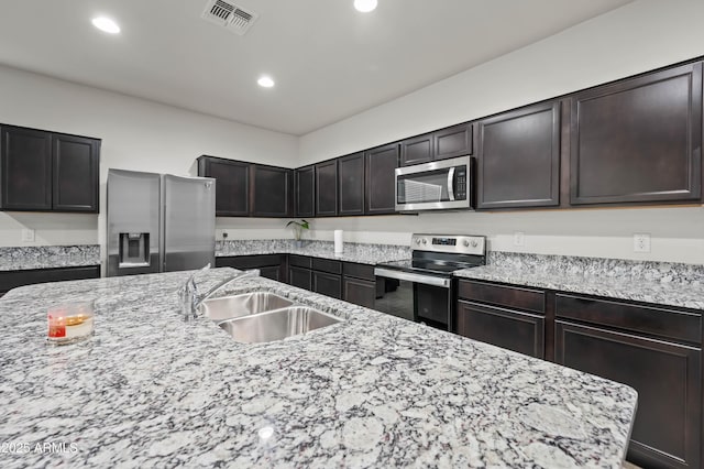 kitchen with a sink, stainless steel appliances, light stone counters, and visible vents