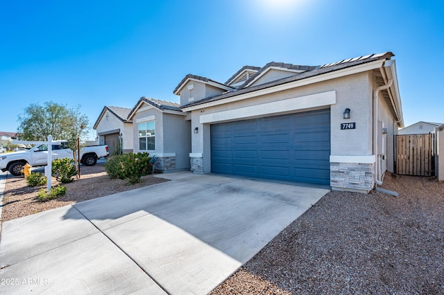 view of front of house with stucco siding, driveway, stone siding, fence, and a garage