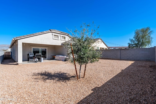 rear view of house with stucco siding, a tile roof, a fenced backyard, and a patio area