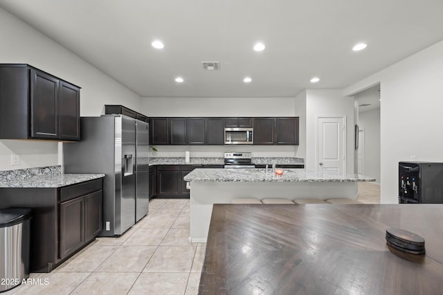 kitchen featuring visible vents, a kitchen bar, appliances with stainless steel finishes, light tile patterned flooring, and light stone countertops