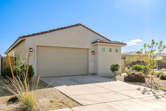 mediterranean / spanish-style home featuring a garage, fence, concrete driveway, a tiled roof, and stucco siding