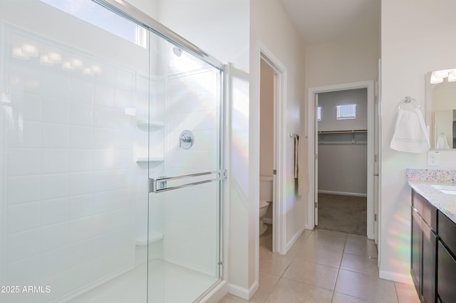 full bath with a walk in closet, toilet, vanity, a shower stall, and tile patterned floors