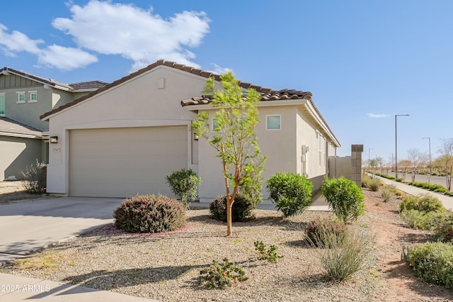 view of front facade with an attached garage, a tile roof, concrete driveway, and stucco siding