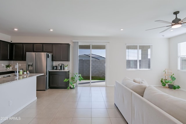 kitchen featuring stainless steel refrigerator with ice dispenser, light tile patterned floors, backsplash, open floor plan, and a sink