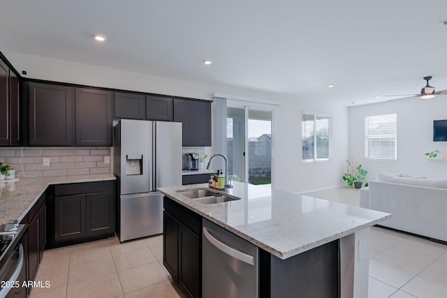 kitchen featuring light stone counters, light tile patterned floors, appliances with stainless steel finishes, open floor plan, and a sink