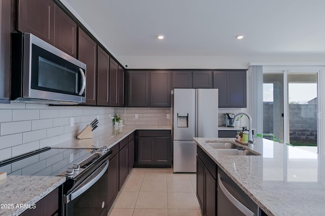 kitchen with light stone counters, dark brown cabinetry, a sink, appliances with stainless steel finishes, and backsplash