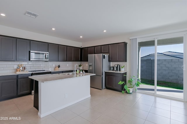 kitchen featuring light stone counters, stainless steel appliances, tasteful backsplash, visible vents, and a sink