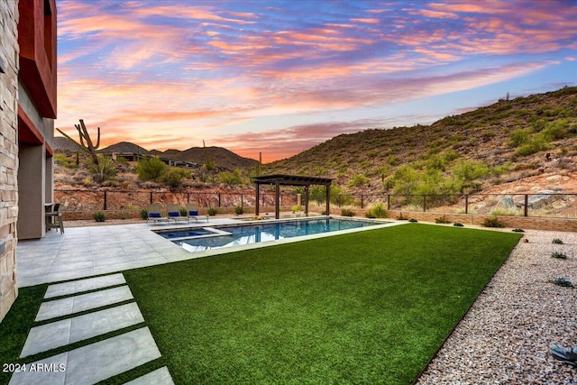 yard at dusk with a mountain view, a patio area, and a pool with hot tub