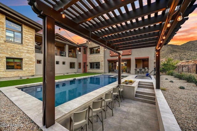 pool at dusk featuring exterior bar, a patio area, a mountain view, and a pergola