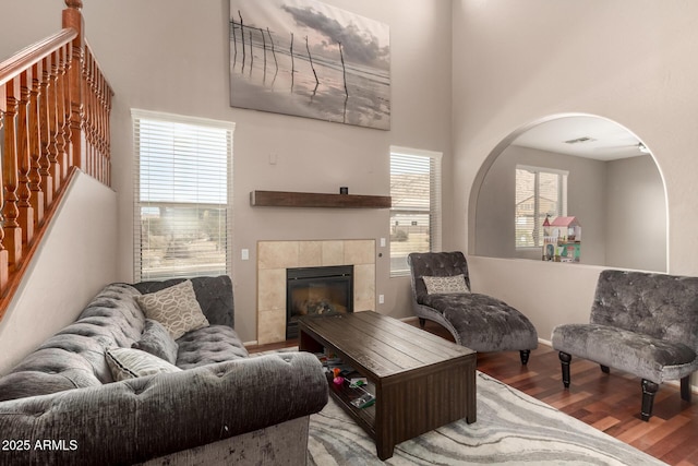 living area with visible vents, stairway, a fireplace, a towering ceiling, and wood finished floors