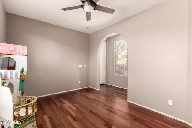 unfurnished room with baseboards, wood finished floors, arched walkways, and ceiling fan