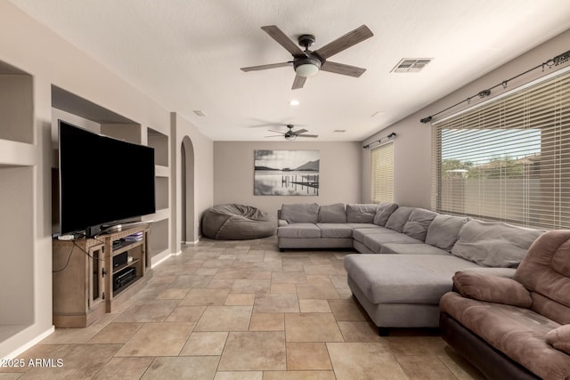 living room featuring built in shelves, arched walkways, visible vents, and ceiling fan