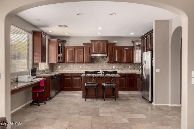 kitchen featuring visible vents, under cabinet range hood, a sink, appliances with stainless steel finishes, and a breakfast bar area