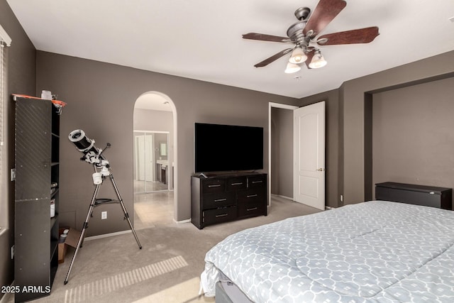 bedroom with baseboards, arched walkways, light carpet, and ceiling fan