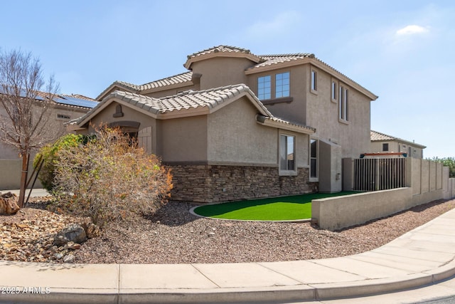 mediterranean / spanish house featuring stone siding, stucco siding, a tiled roof, and fence