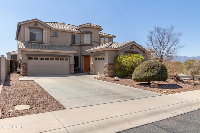 mediterranean / spanish house featuring fence, a tiled roof, concrete driveway, stucco siding, and stone siding