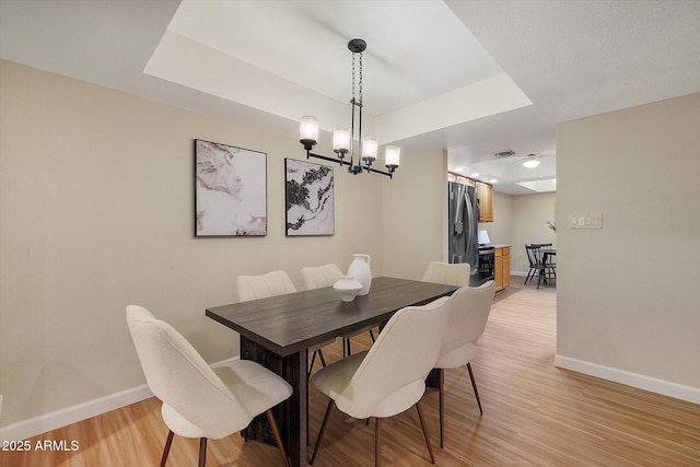 dining space featuring light wood finished floors, baseboards, and a tray ceiling