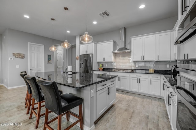 kitchen with wall chimney range hood, appliances with stainless steel finishes, white cabinetry, hanging light fixtures, and a kitchen island