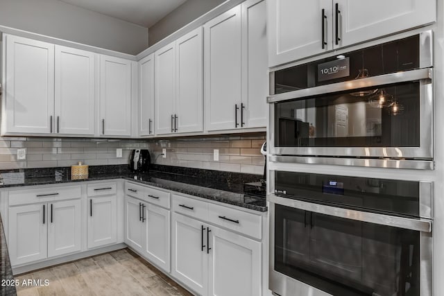 kitchen featuring dark stone countertops, white cabinets, double oven, and decorative backsplash