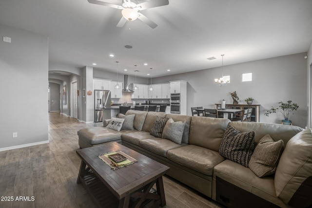 living room with ceiling fan with notable chandelier and dark hardwood / wood-style flooring