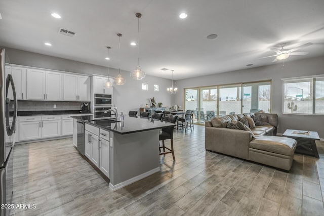 kitchen with pendant lighting, sink, a kitchen island with sink, white cabinets, and a kitchen bar