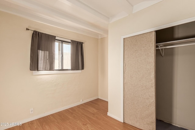 unfurnished bedroom featuring hardwood / wood-style floors, a closet, and beamed ceiling