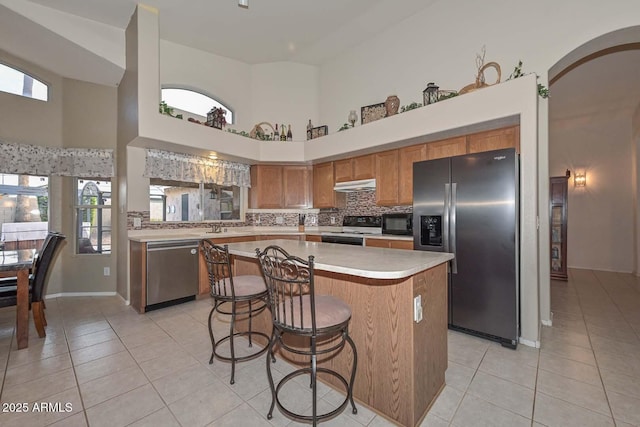 kitchen featuring light tile patterned floors, a towering ceiling, appliances with stainless steel finishes, and tasteful backsplash