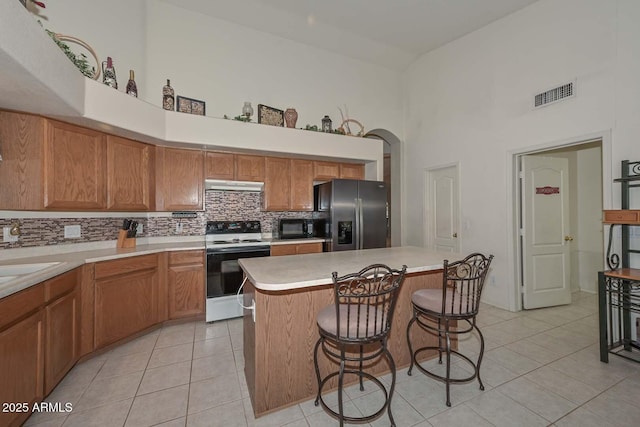 kitchen with a high ceiling, stainless steel refrigerator with ice dispenser, white electric range oven, a kitchen island, and a breakfast bar area