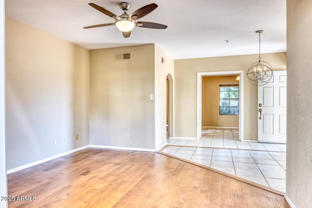 unfurnished room featuring arched walkways, a ceiling fan, wood finished floors, a chandelier, and baseboards