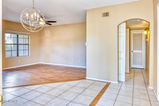 empty room featuring arched walkways, a chandelier, baseboards, and light tile patterned floors