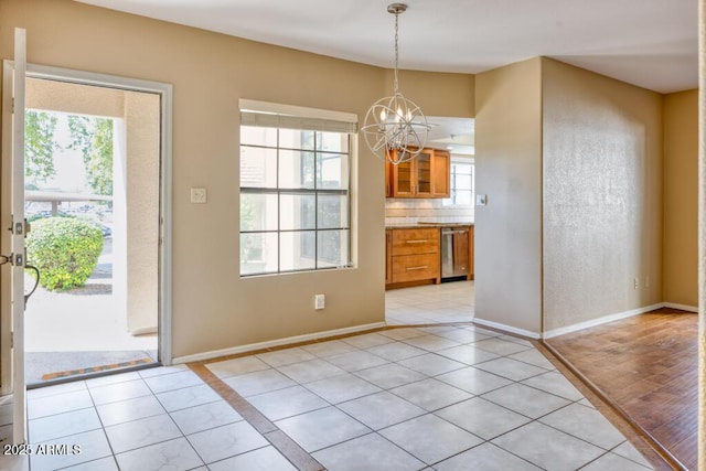 unfurnished dining area featuring a chandelier, light tile patterned floors, plenty of natural light, and baseboards