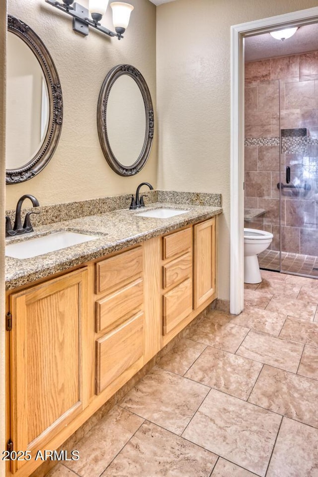 full bathroom featuring a stall shower, a textured wall, toilet, and double vanity