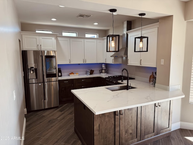 kitchen with a peninsula, a sink, visible vents, wall chimney range hood, and stainless steel fridge