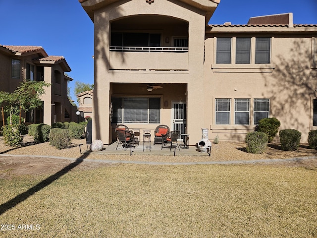 back of house featuring a lawn, a patio area, a balcony, and stucco siding