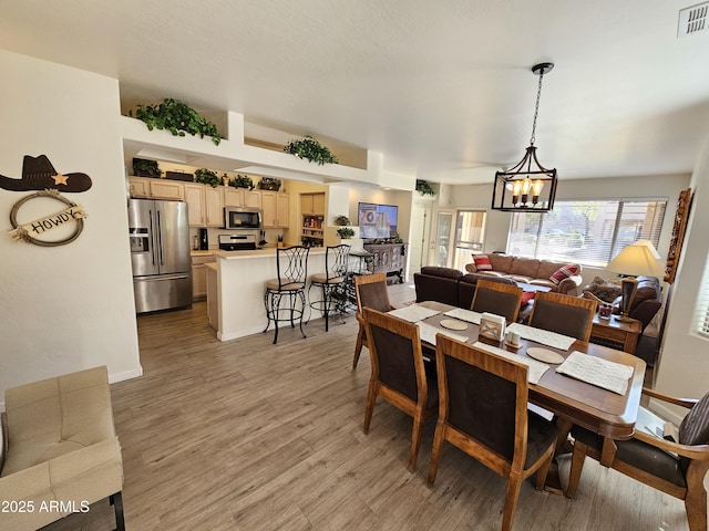 dining room with baseboards, light wood-style flooring, visible vents, and a notable chandelier