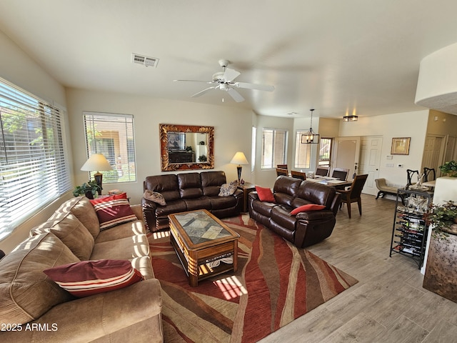 living room with ceiling fan with notable chandelier, visible vents, and wood finished floors