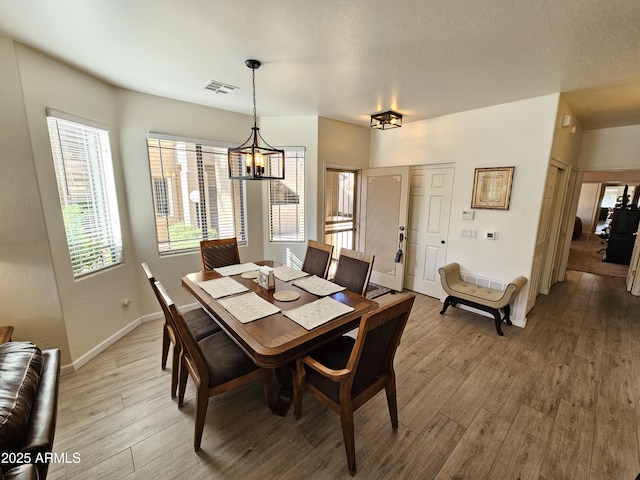 dining space with light wood-type flooring, visible vents, baseboards, and a textured ceiling