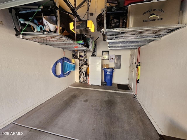 garage featuring electric panel, baseboards, a garage door opener, and freestanding refrigerator