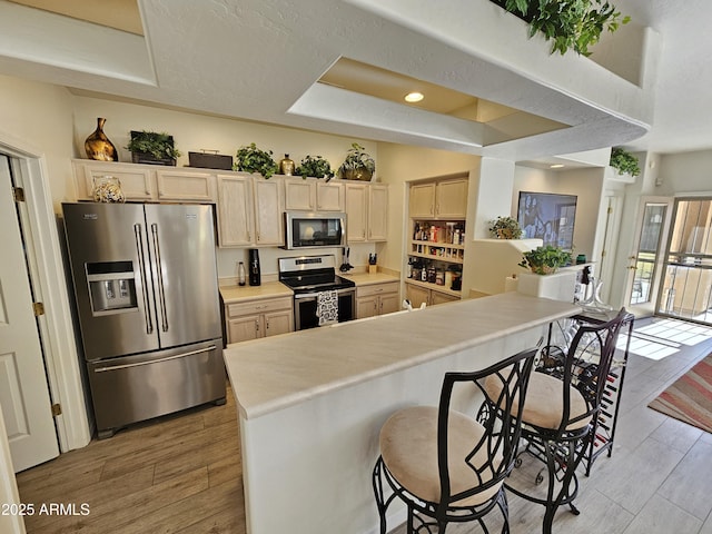 kitchen featuring light wood-type flooring, a breakfast bar area, appliances with stainless steel finishes, and a tray ceiling