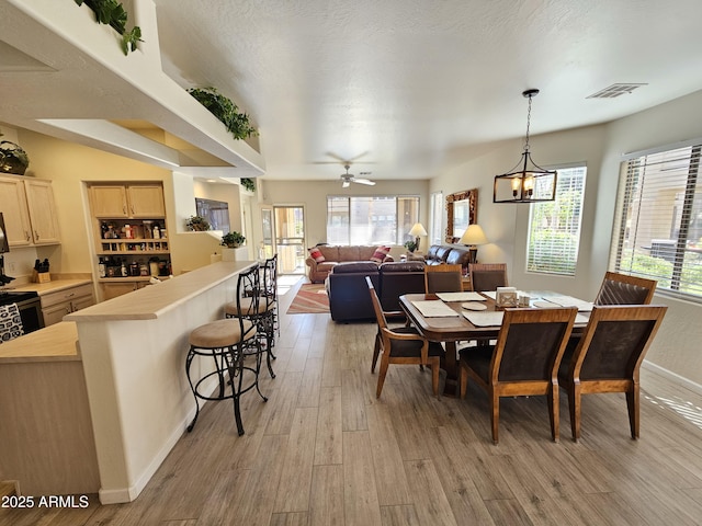 dining room with visible vents, light wood-style flooring, a textured ceiling, baseboards, and ceiling fan with notable chandelier