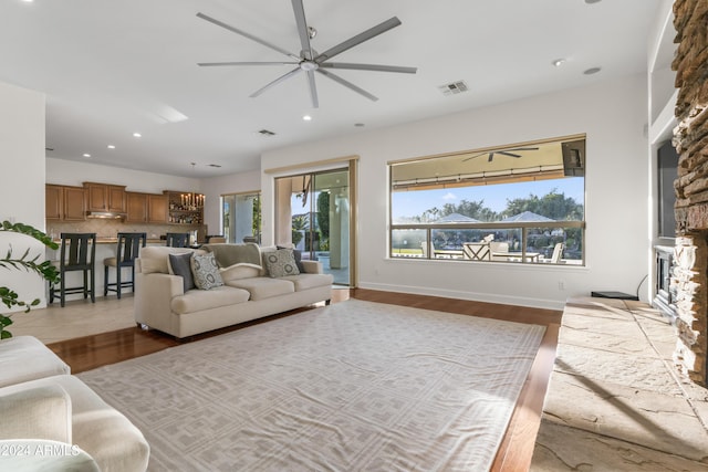 living room with a fireplace, ceiling fan, light hardwood / wood-style flooring, and a healthy amount of sunlight