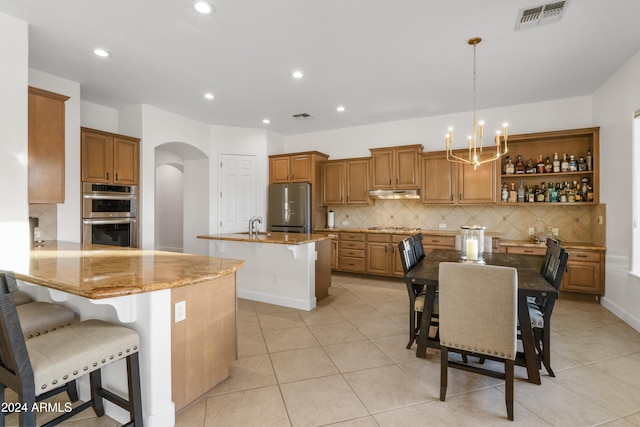 kitchen featuring light stone counters, kitchen peninsula, stainless steel appliances, an island with sink, and a kitchen bar