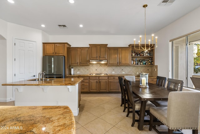 kitchen featuring a kitchen breakfast bar, a kitchen island with sink, stainless steel appliances, pendant lighting, and backsplash