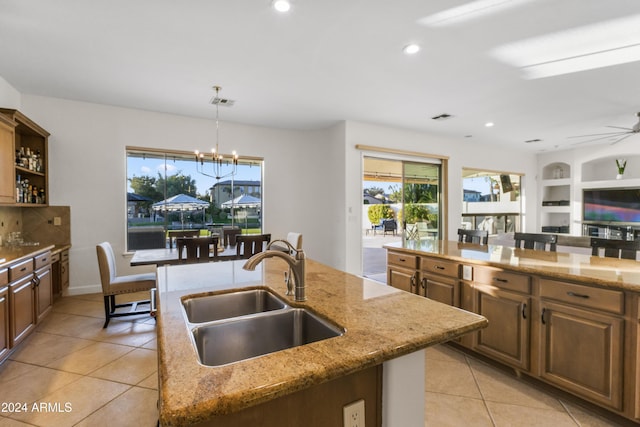 kitchen featuring sink, ceiling fan with notable chandelier, a kitchen island with sink, and light stone countertops