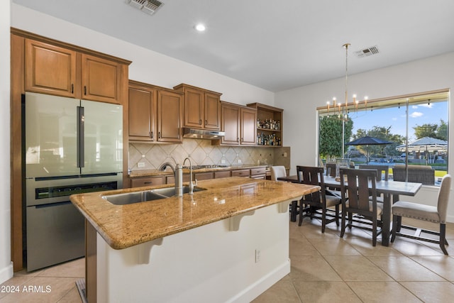 kitchen with light tile patterned floors, a kitchen bar, a kitchen island with sink, white refrigerator, and sink