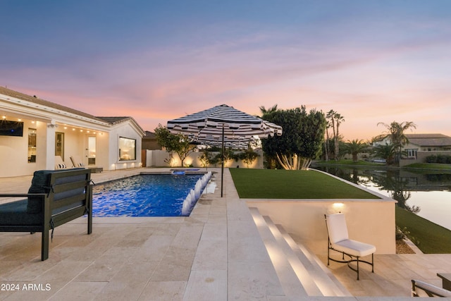 pool at dusk featuring pool water feature, a yard, a water view, and a patio