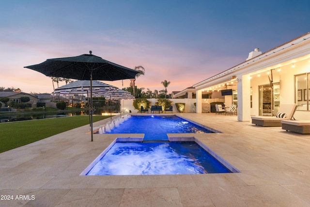 pool at dusk with a patio and an in ground hot tub