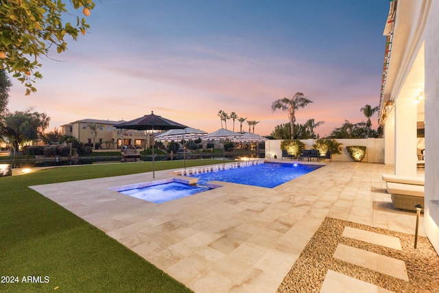 pool at dusk featuring a lawn, a patio area, and an in ground hot tub