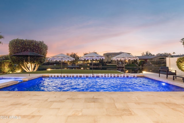 pool at dusk featuring pool water feature and a patio area