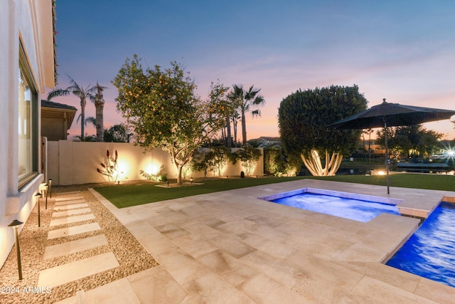 pool at dusk featuring a patio area, an in ground hot tub, and a yard